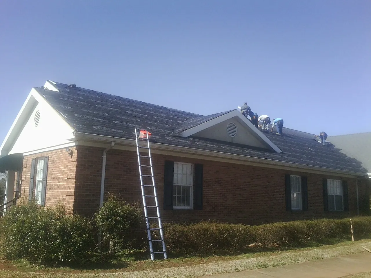 Crew tearing shingles off a brick ranch roof with a ladder set — Emergency Roof Repair work by our crew in San Rafael