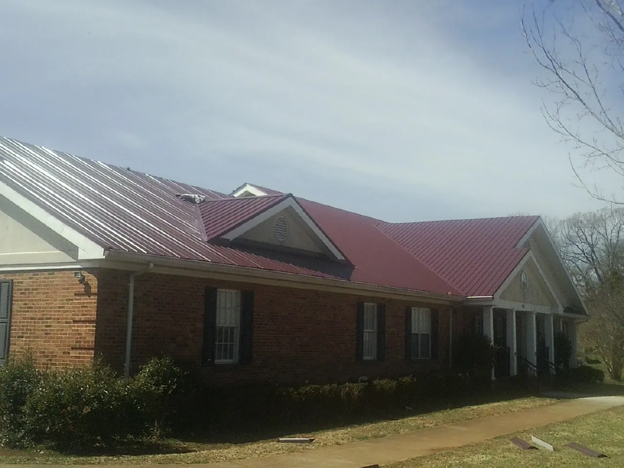 Red metal roof with gabled entries on a long brick building, from a Hail Damage Roof Repair job in San Rafael