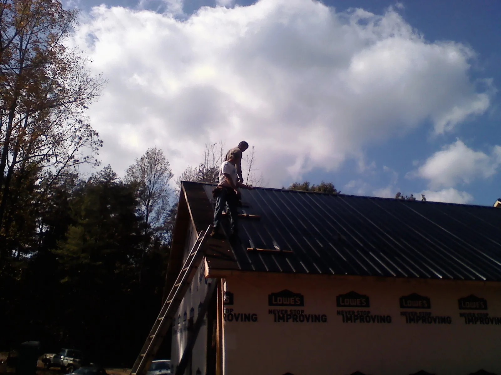 Roofer fastening dark metal panels high against a cloudy sky, from a Roof Inspection job in San Rafael