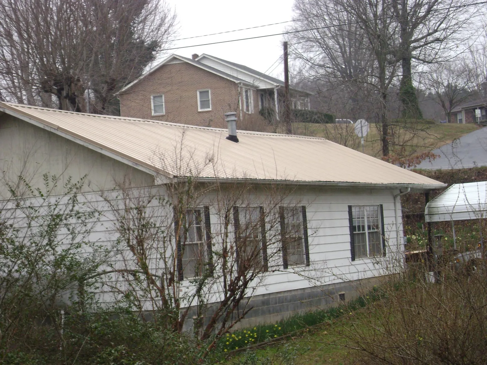 Tan metal roof on a white sided house set into a hillside — Commercial Roofing by Roofing Brothers in San Rafael